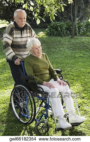 Picture - Man pushing his disabled wife's wheelchair in a garden. Fotosearch