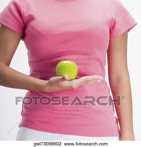 Stock Image - Mid section view of a woman holding a green apple. Fotosearch
