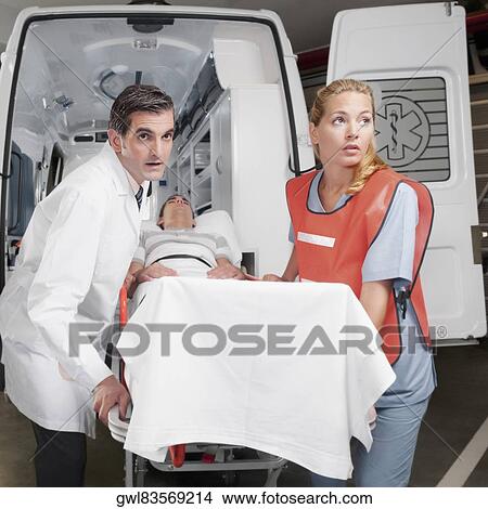 Paramedics leading a patient on a gurney from an ambulance View Large Photo Image Picture - Paramedics leading a patient on a gurney from an ambulance. Fotosearch