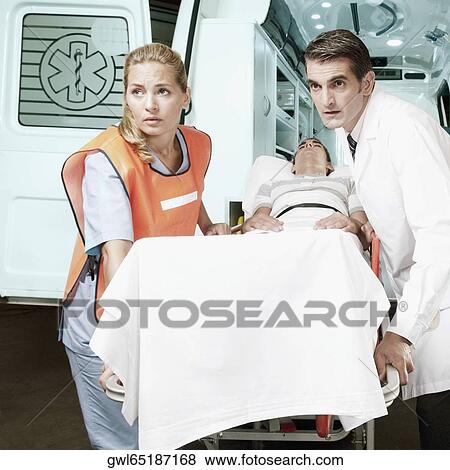 Paramedics pushing a patient on a gurney from an ambulance View Large Photo Image Stock Photo - Paramedics pushing a patient on a gurney from an ambulance. Fotosearch