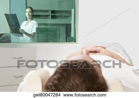 Picture - Patient going through an MRI scan with a doctor analyzing an X-Ray report in background. Fotosearch