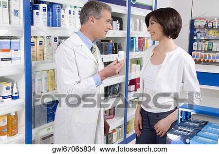 Pharmacist holding a medicine bottle and consulting with customer View Large Photo Image Picture - Pharmacist holding a medicine bottle and consulting with customer. Fotosearch
