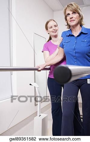 Stock Image - Physiotherapist assisting a patient in walking. Fotosearch