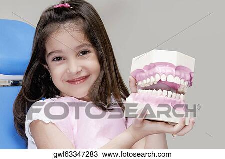 Stock Image - Portrait of a girl holding a set of dentures. Fotosearch