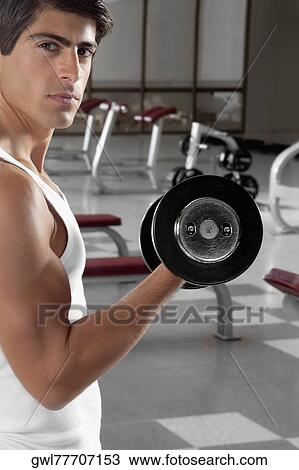 Stock Image - Portrait of a man exercising with dumbbell in a gym. Fotosearch