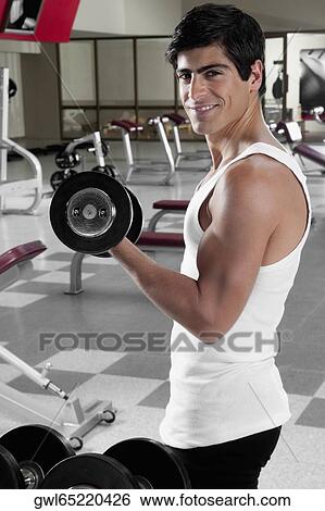 Portrait of a man exercising with dumbbell in a gym View Large Photo Image Stock Photograph - Portrait of a man exercising with dumbbell in a gym. Fotosearch