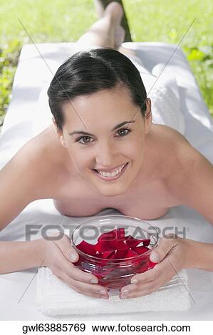 Stock Photo - Portrait of a woman lying on a massage table holding a bowl of rose petals. Fotosearch