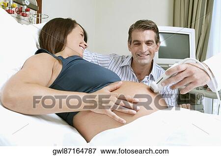 Pregnant woman going through an ultrasound scan with her husband beside her View Large Photo Image Stock Photo - Pregnant woman going through an ultrasound scan with her husband beside her. Fotosearch
