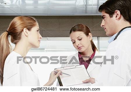 Three doctors discussing a report View Large Photo Image Stock Image - Three doctors discussing a report. Fotosearch
