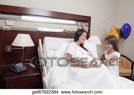 Picture - Woman carrying her newborn baby with her daughter in a hospital. Fotosearch