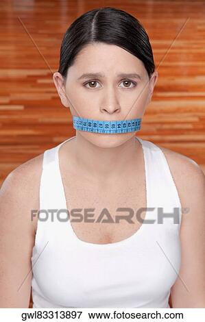 Woman covering her mouth with a tape measure View Large Photo Image Stock Photo - Woman covering her mouth with a tape measure. Fotosearch