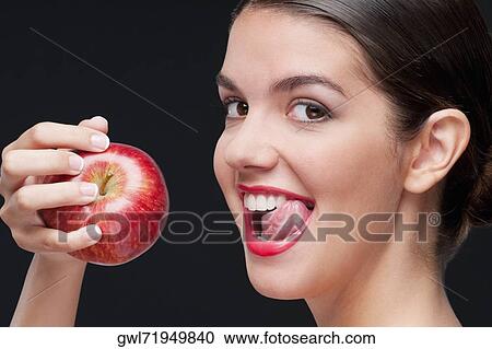 Stock Image - Woman eating a red apple and licking lips. Fotosearch