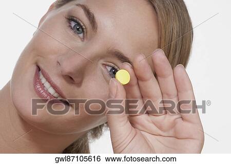 Woman holding a pill in front of her eye View Large Photo Image Stock Photograph - Woman holding a pill in front of her eye. Fotosearch