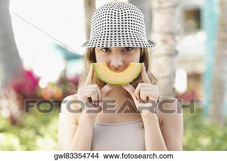Woman holding a slice of melon in front of her mouth View Large Photo Image Picture - Woman holding a slice of melon in front of her mouth. Fotosearch