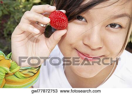 Stock Image - Woman holding a strawberry and smirking. Fotosearch
