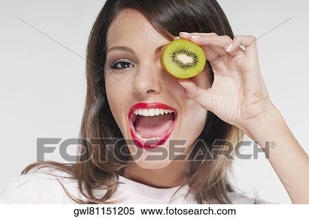 Woman holding half a kiwi over her eye View Large Photo Image Stock Photography - Woman holding half a kiwi over her eye. Fotosearch