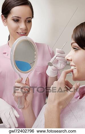 Woman looking into a mirror in dentist's office View Large Photo Image Stock Photograph - Woman looking into a mirror in dentist's office. Fotosearch