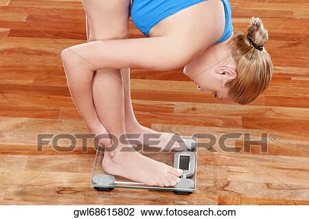 Stock Image - Woman measuring her weight on a weighing scale. Fotosearch