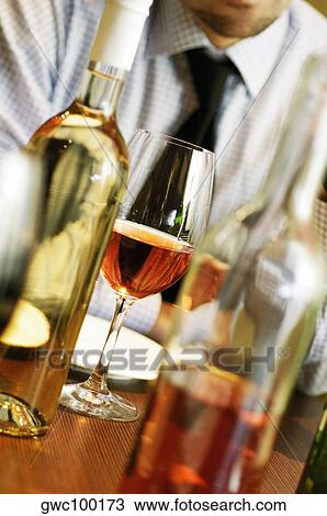 Stock Image - Close-up of a man sitting with a glass of wine and wine bottles. Fotosearch