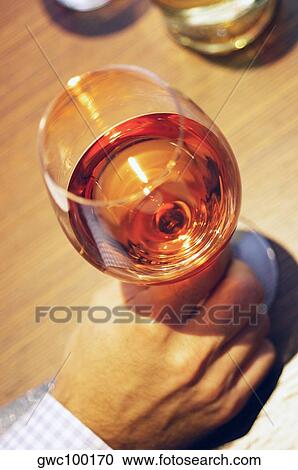 Stock Image - High angle view of a person's hand holding a glass of wine. Fotosearch