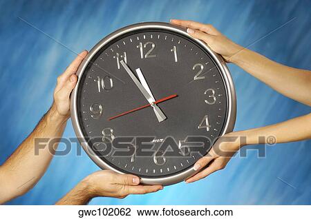 Stock Image - Close-up of a man and a woman's hands holding a clock. Fotosearch
