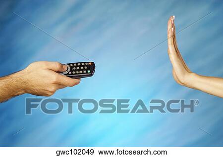 Stock Photo - Man's hand holding a remote control with a woman's hand making a stop gesture. Fotosearch