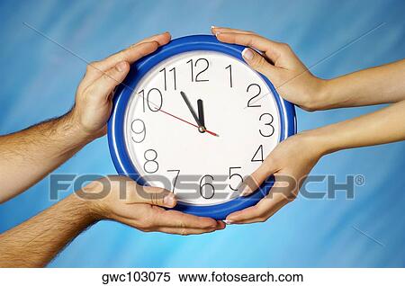 Stock Photography - Close-up of a man and a woman's hands holding a clock. Fotosearch