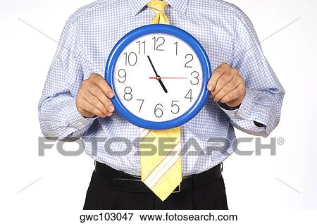 Mid section view of a businessman holding a clock View Large Photo Image Stock Photo - Mid section view of a businessman holding a clock. Fotosearch