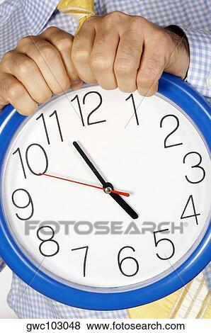 Stock Photo - Mid section view of a businessman holding a clock. Fotosearch