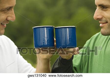 Stock Image - Close-up of a mid adult man and a mature man toasting with mugs. Fotosearch