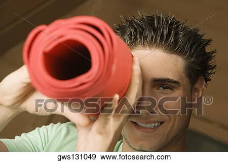 Portrait of a young man looking through a rolled up exercise mat View Large Photo Image Stock Photo - Portrait of a young man looking through a rolled up exercise mat. Fotosearch