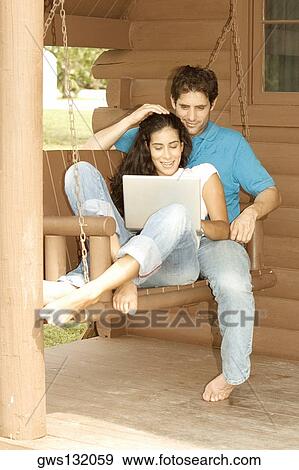 Mid adult man and a young woman sitting on a porch swing with a laptop View Large Photo Image Stock Photo - Mid adult man and a young woman sitting on a porch swing with a laptop. Fotosearch