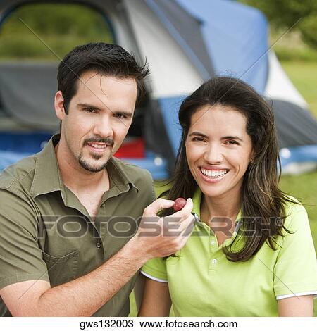 Stock Image - Portrait of a young man feeding a young woman berry fruit. Fotosearch