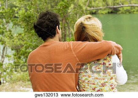 Rear view of a mid adult man sitting with his arm around a young woman View Large Photo Image Stock Image - Rear view of a mid adult man sitting with his arm around a young woman. Fotosearch