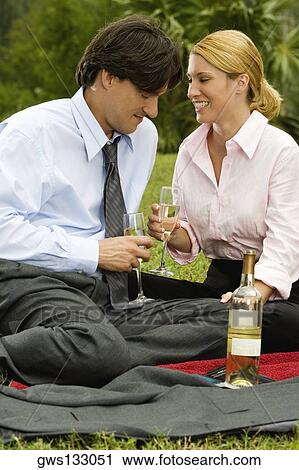 Stock Image - Businessman and a businesswoman sitting in the park holding champagne flutes. Fotosearch