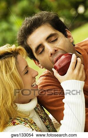 Close-up of a young woman feeding an apple to a mid adult man View Large Photo Image Picture - Close-up of a young woman feeding an apple to a mid adult man. Fotosearch