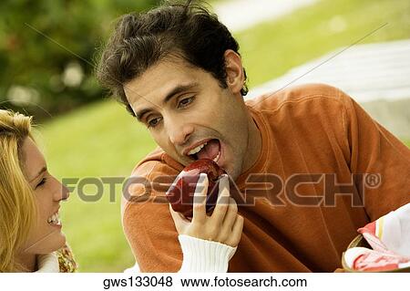 Close-up of a young woman feeding an apple to a mid adult man View Large Photo Image Stock Photo - Close-up of a young woman feeding an apple to a mid adult man. Fotosearch