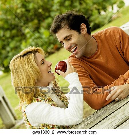 Stock Image - Mid adult man sitting with a young woman eating an apple. Fotosearch