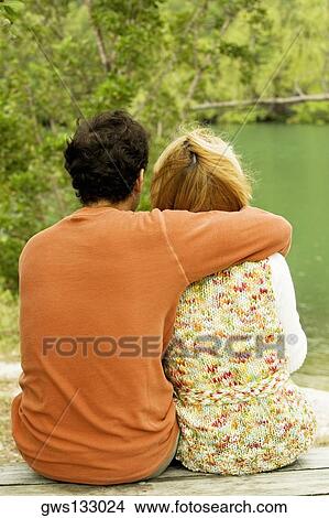 Rear view of a mid adult man sitting with his arm around a young woman View Large Photo Image Picture - Rear view of a mid adult man sitting with his arm around a young woman. Fotosearch