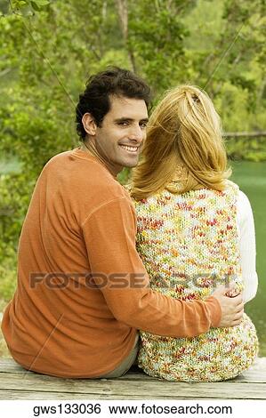 Rear view of a mid adult man sitting with his arm around a young woman View Large Photo Image Stock Photograph - Rear view of a mid adult man sitting with his arm around a young woman. Fotosearch