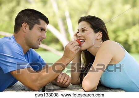 Stock Photo - Side profile of a mid adult man feeding a young woman a strawberry. Fotosearch