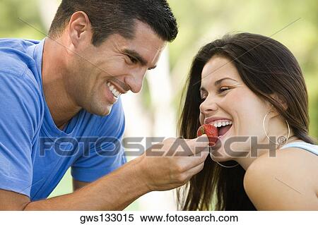 Stock Photography - Side profile of a mid adult man feeding a young woman a strawberry. Fotosearch