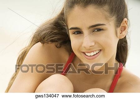 Stock Photo - Portrait of a girl sitting on the beach smiling. Fotosearch