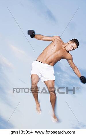 Low angle view of a young man jumping with his arms outstretched View Large Photo Image Picture - Low angle view of a young man jumping with his arms outstretched. Fotosearch