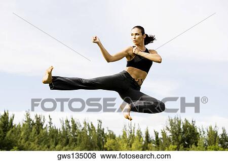Low angle view of a young woman practicing martial arts View Large Photo Image Stock Photo - Low angle view of a young woman practicing martial arts. Fotosearch