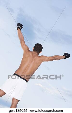 Rear view of a young man standing with his arms raised View Large Photo Image Stock Photography - Rear view of a young man standing with his arms raised. Fotosearch