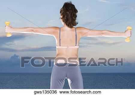Stock Photograph - Rear view of a young woman exercising with dumbbells. Fotosearch