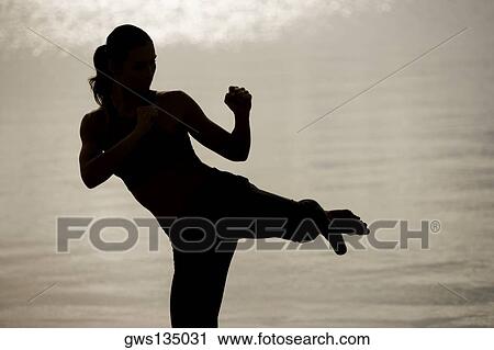 Stock Image - Silhouette of a young woman practicing martial arts on the beach. Fotosearch