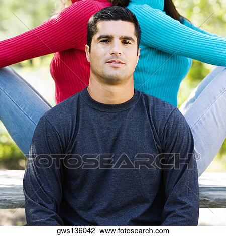 Stock Image - Portrait of a young man with two women sitting back to back behind him. Fotosearch