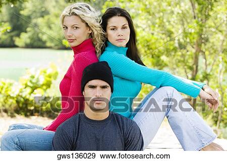 Stock Photo - Portrait of a young man with two young women sitting back to back behind him. Fotosearch